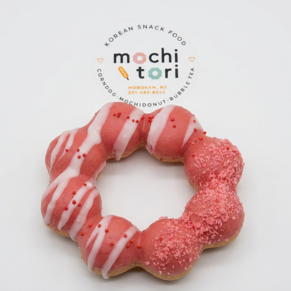 Pink Mochi Tori donut topped with white icing stripes, red sprinkles, and textured pink sugar coating.